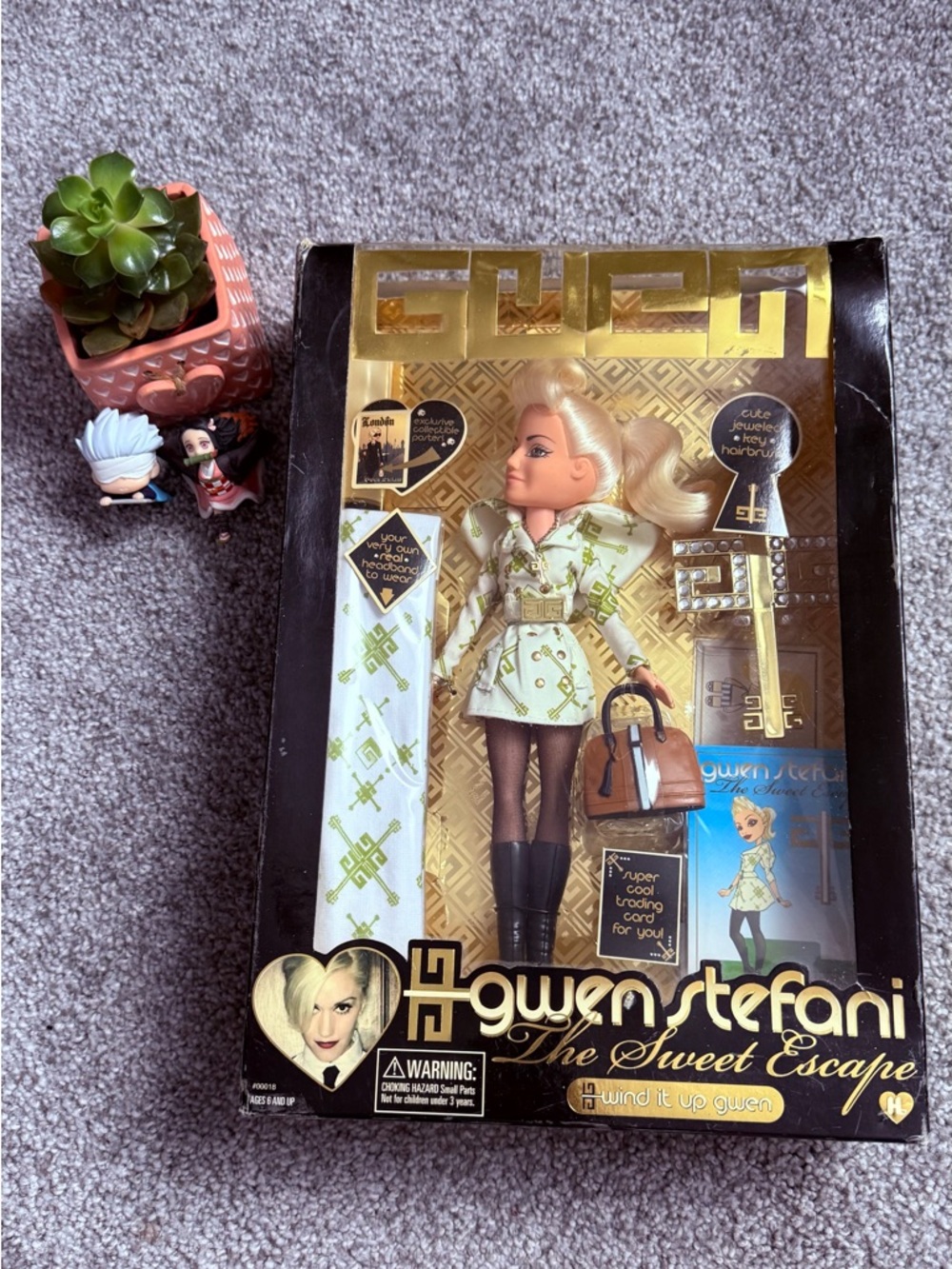 GX by Gwen Stefani Blonde Doll in Green Patterned Trench Coat with Brown Handbag